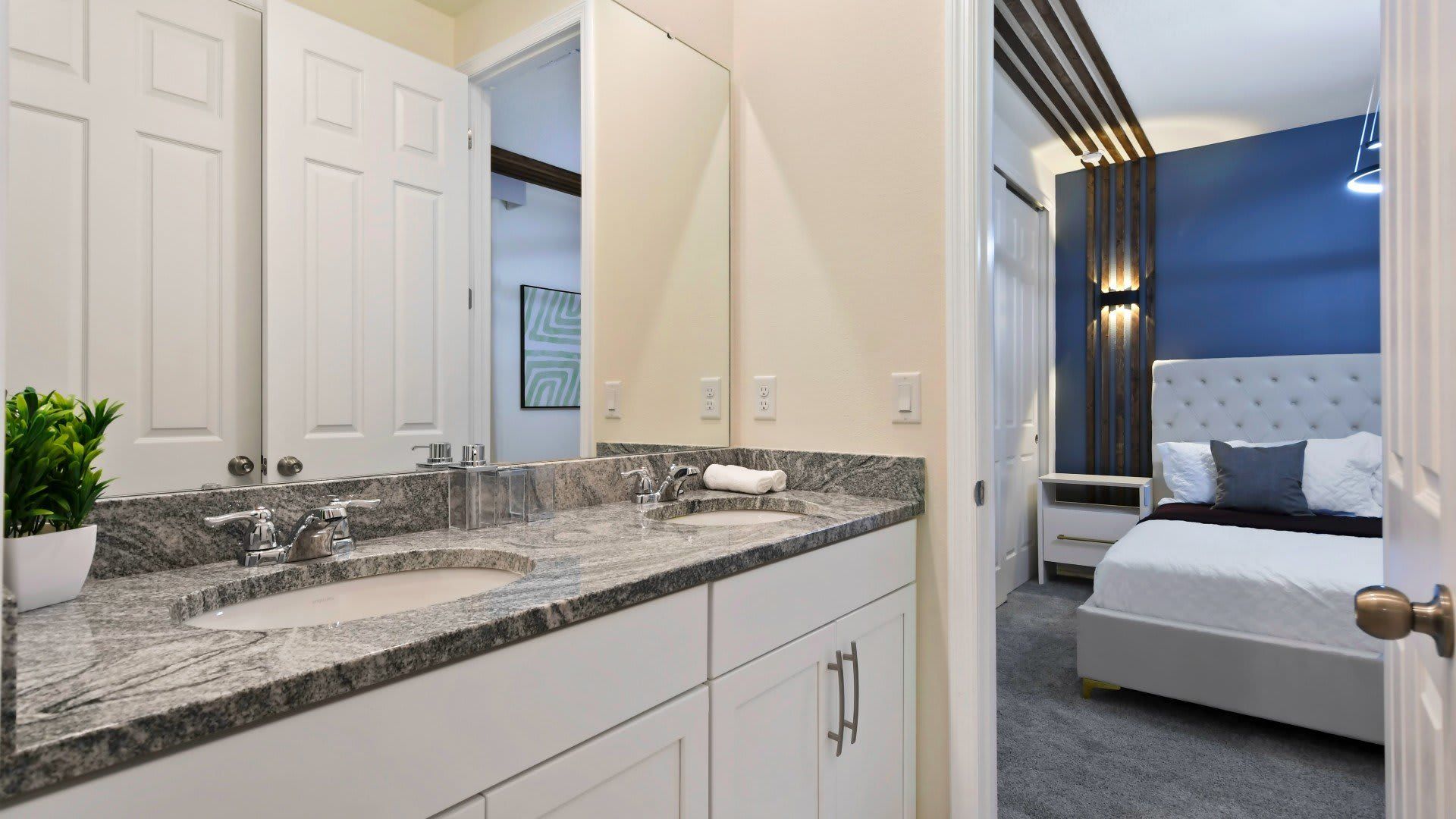 Elegant bathroom with dual granite-topped sinks, leading into a cozy bedroom.