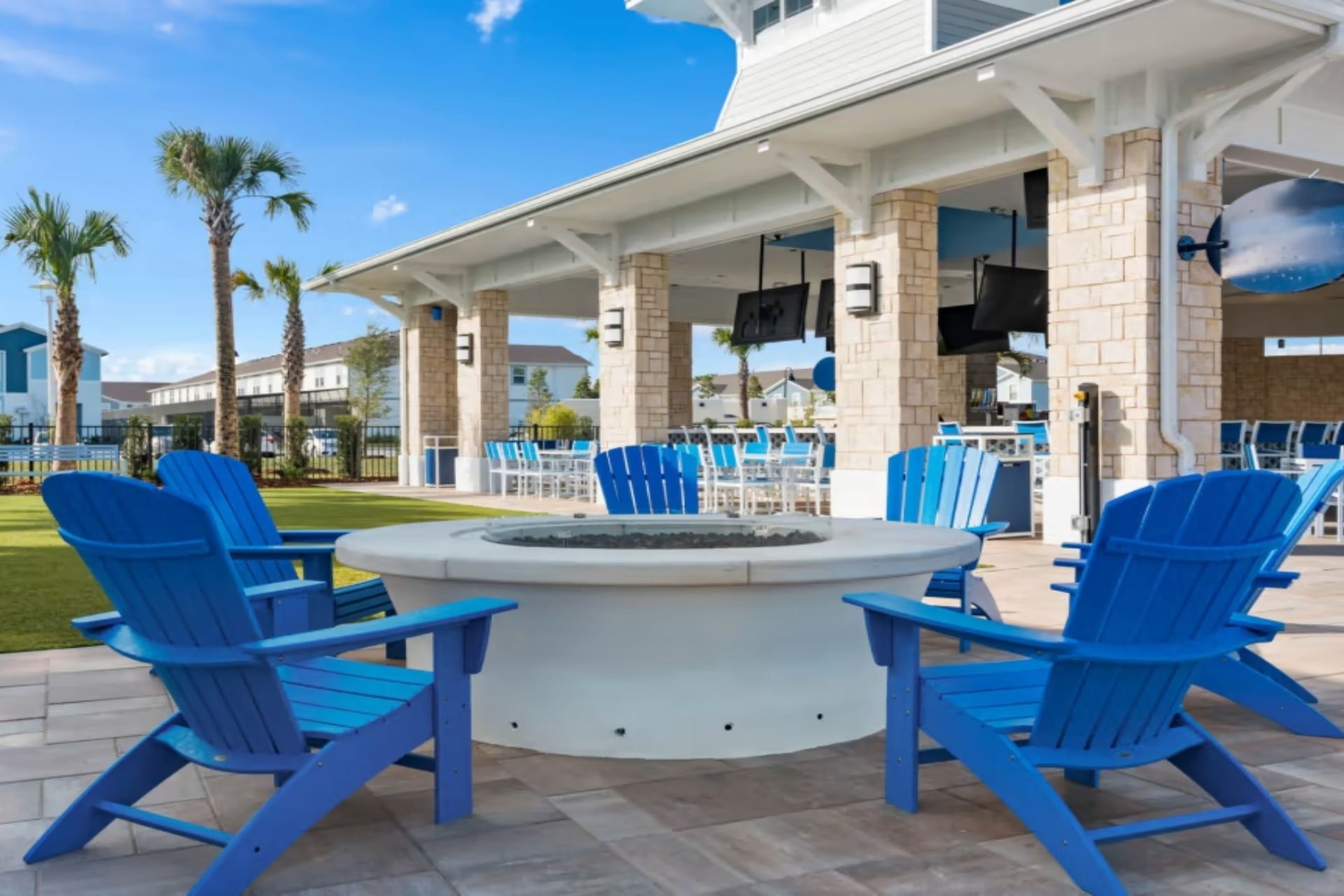 Cozy fire pit lounge with bright blue chairs, perfect for relaxing under the palms and open sky.