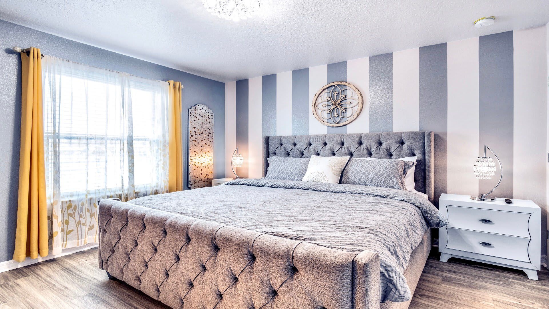 Elegant bedroom with striped walls, tufted headboard, and bright accents for a chic, relaxing retreat.