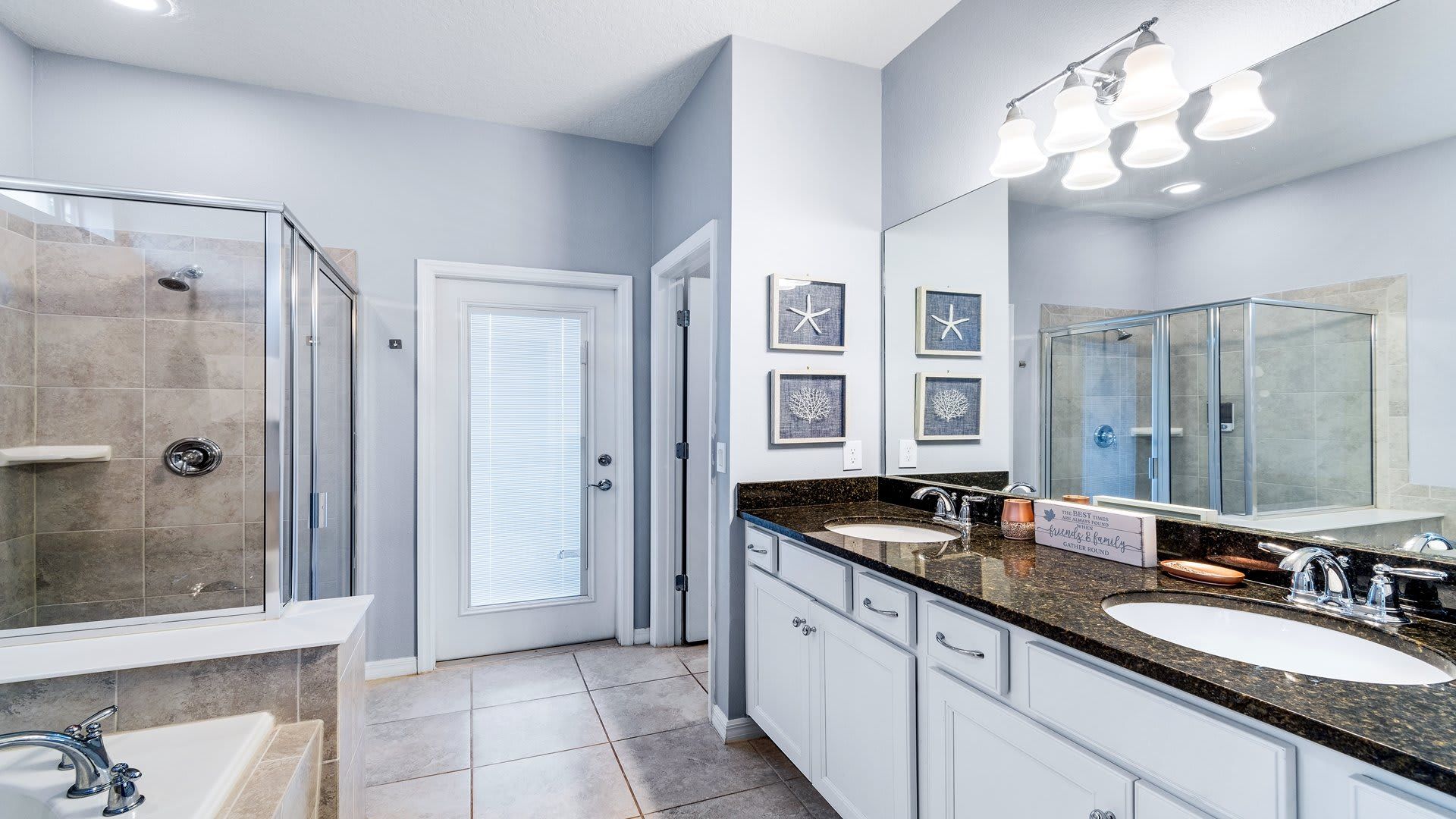 Elegant bathroom with granite counters, dual sinks, a glass shower, and serene coastal decor.