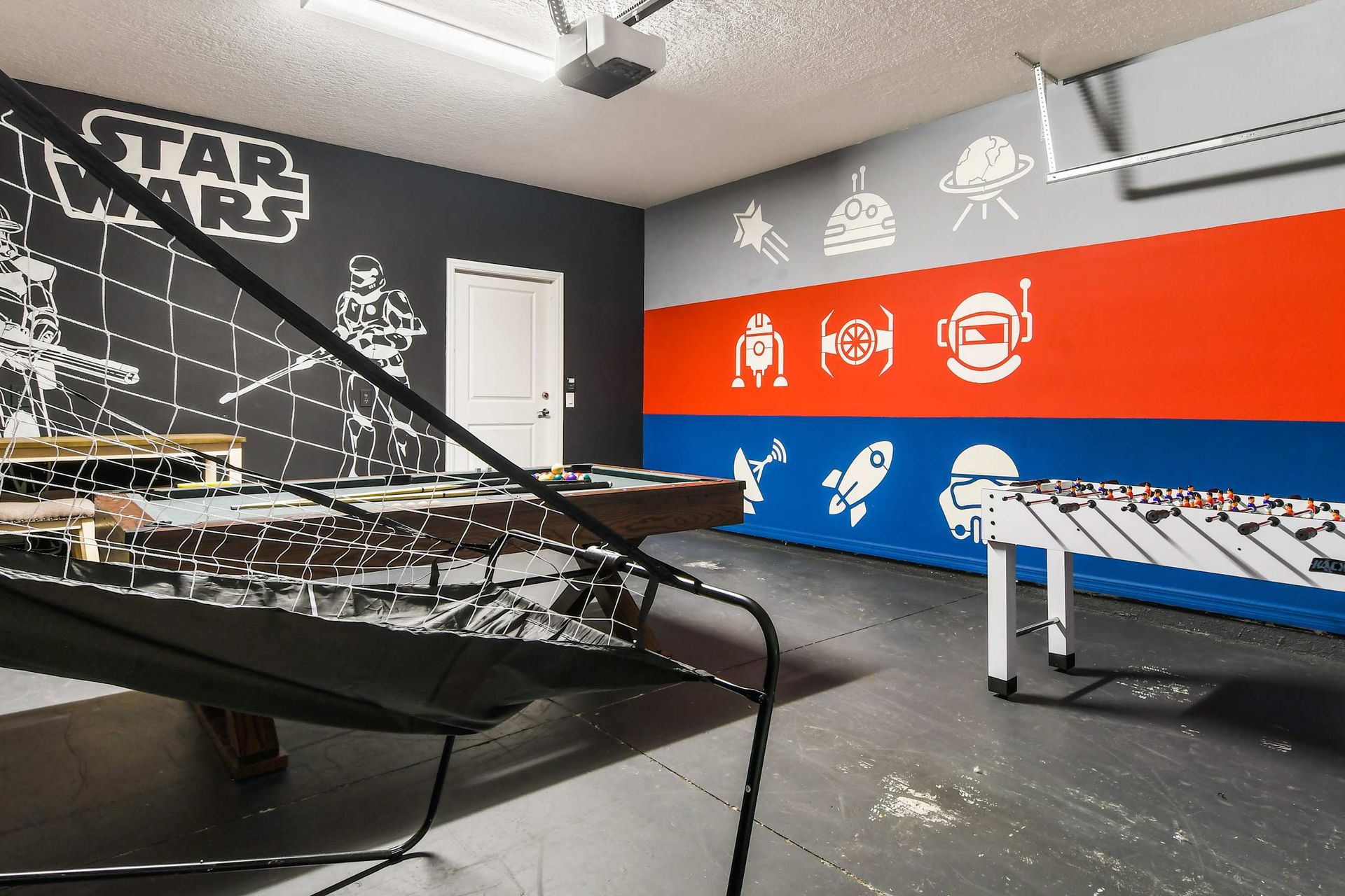 Space-themed game room with foosball, basketball arcade, pool table, and colorful wall art. Fun awaits!