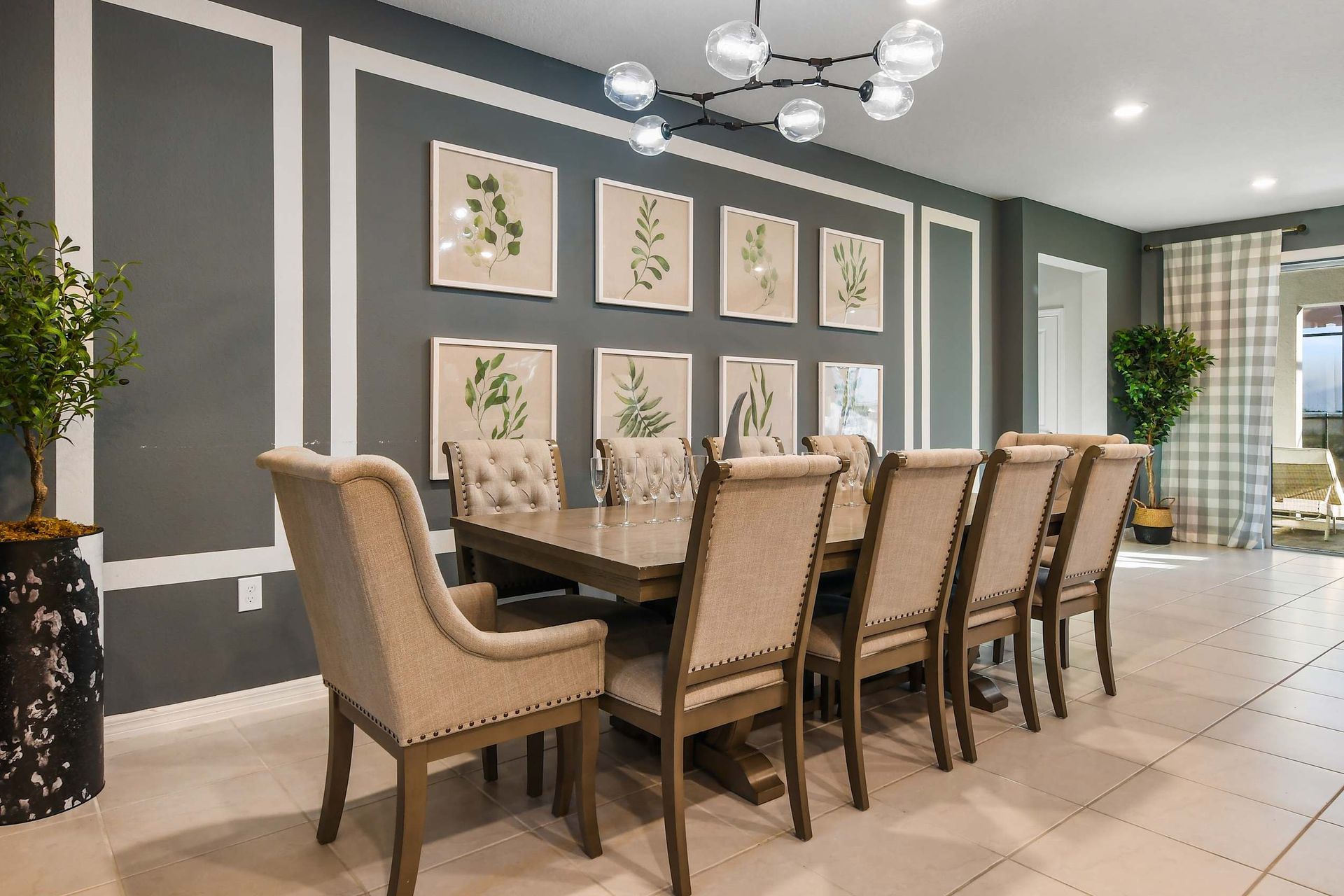 Spacious dining area with a long table, upholstered chairs, modern chandelier, and nature-inspired decor.