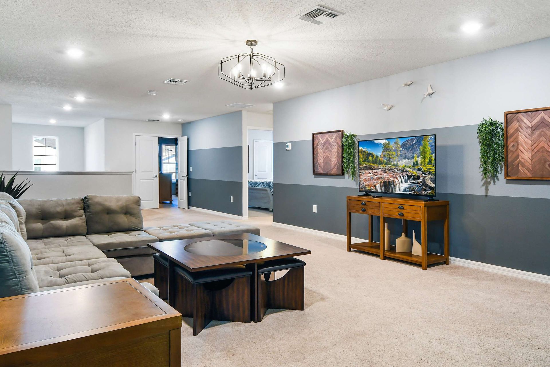 Spacious upstairs lounge with comfy sectional, large TV, modern decor, and plenty of natural light.