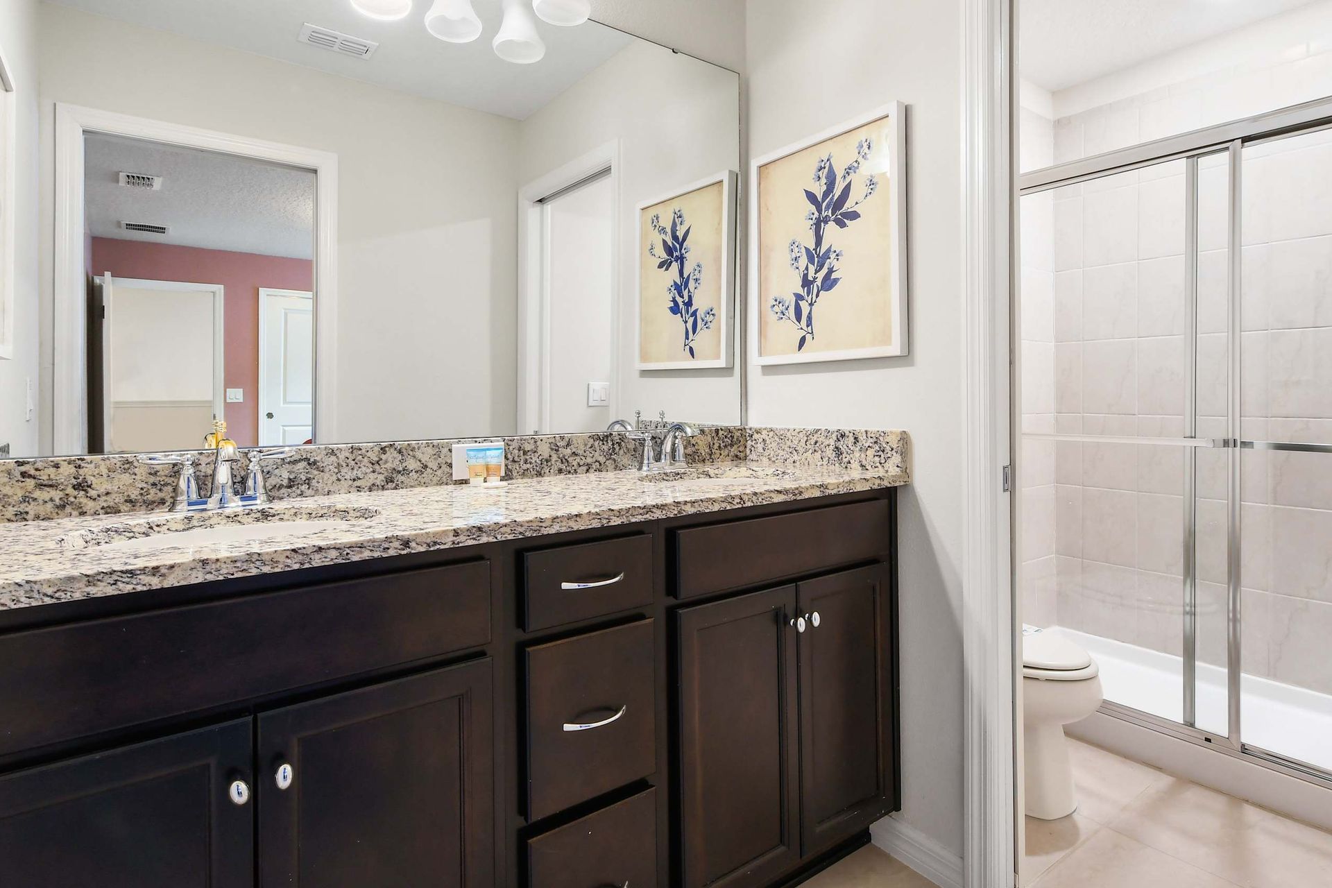 Bright bathroom with granite vanity, framed art, and a sleek glass-enclosed shower.
