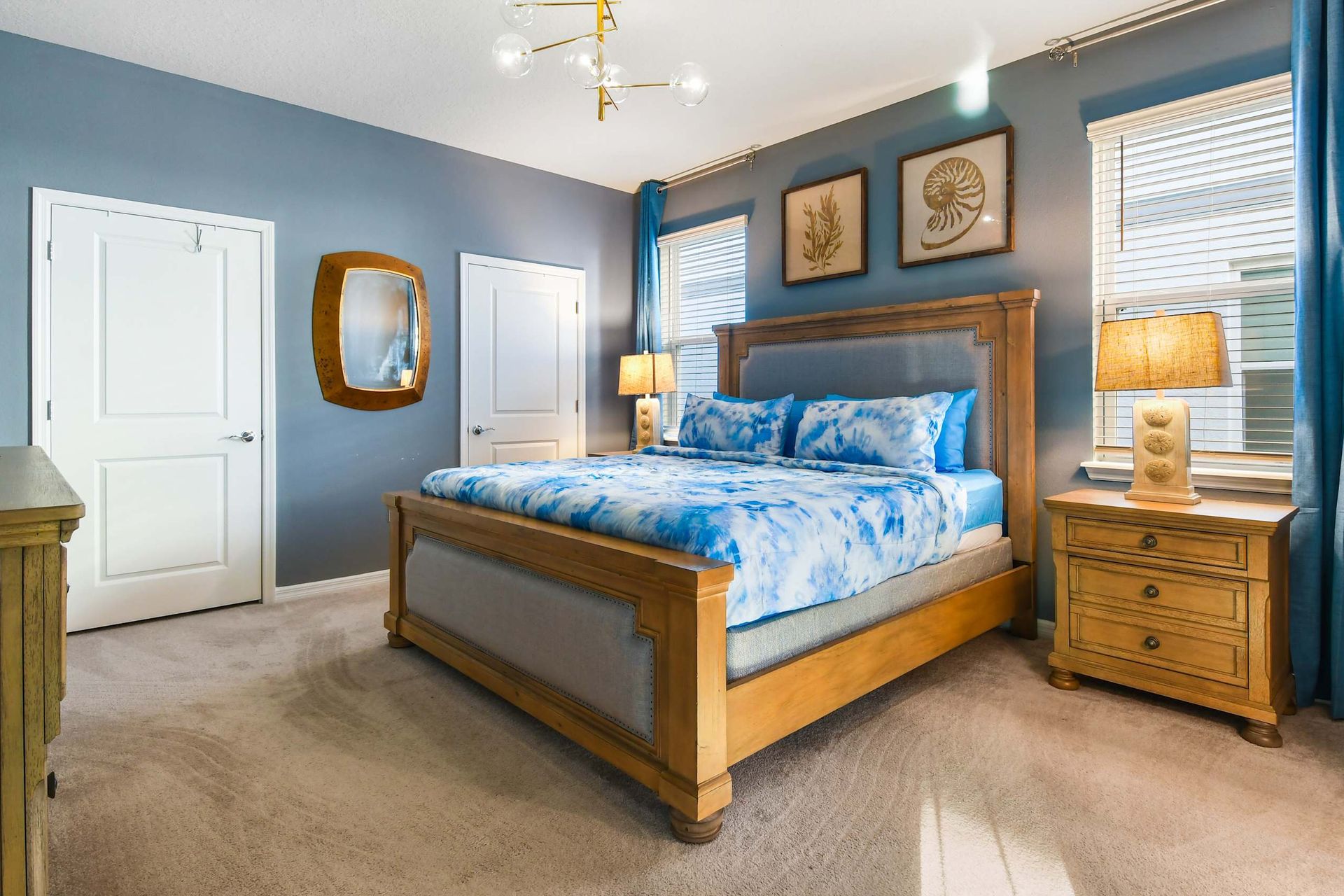 Elegant master bedroom with a king bed, chic blue decor, ample natural light, and a large smart TV.