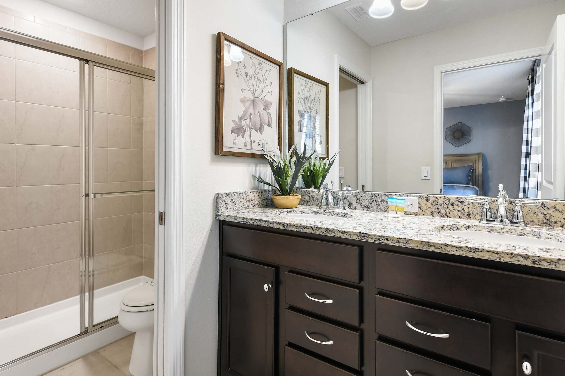 Stylish bathroom with granite double vanity, framed art, and a sleek glass-enclosed shower.