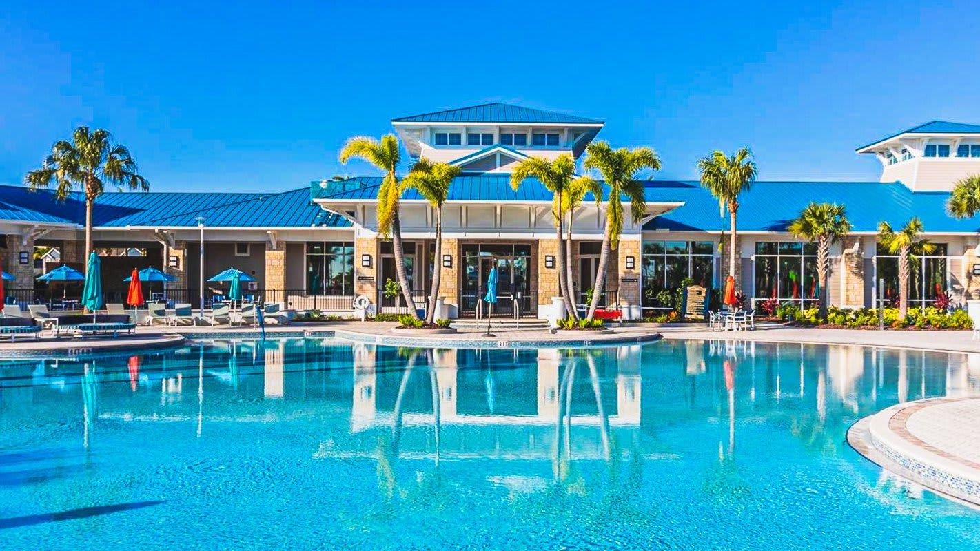 Resort-style clubhouse with a large pool, sun loungers, and tropical palm trees.