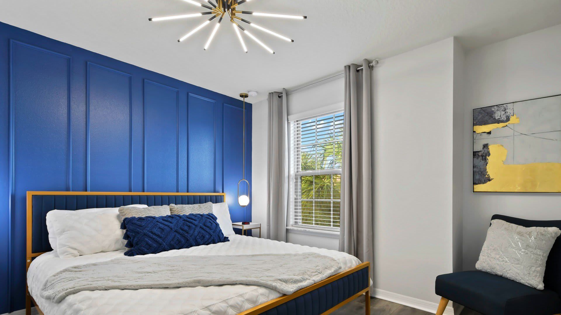 Elegant bedroom with bold blue accents, modern lighting & cozy, luxurious bedding!