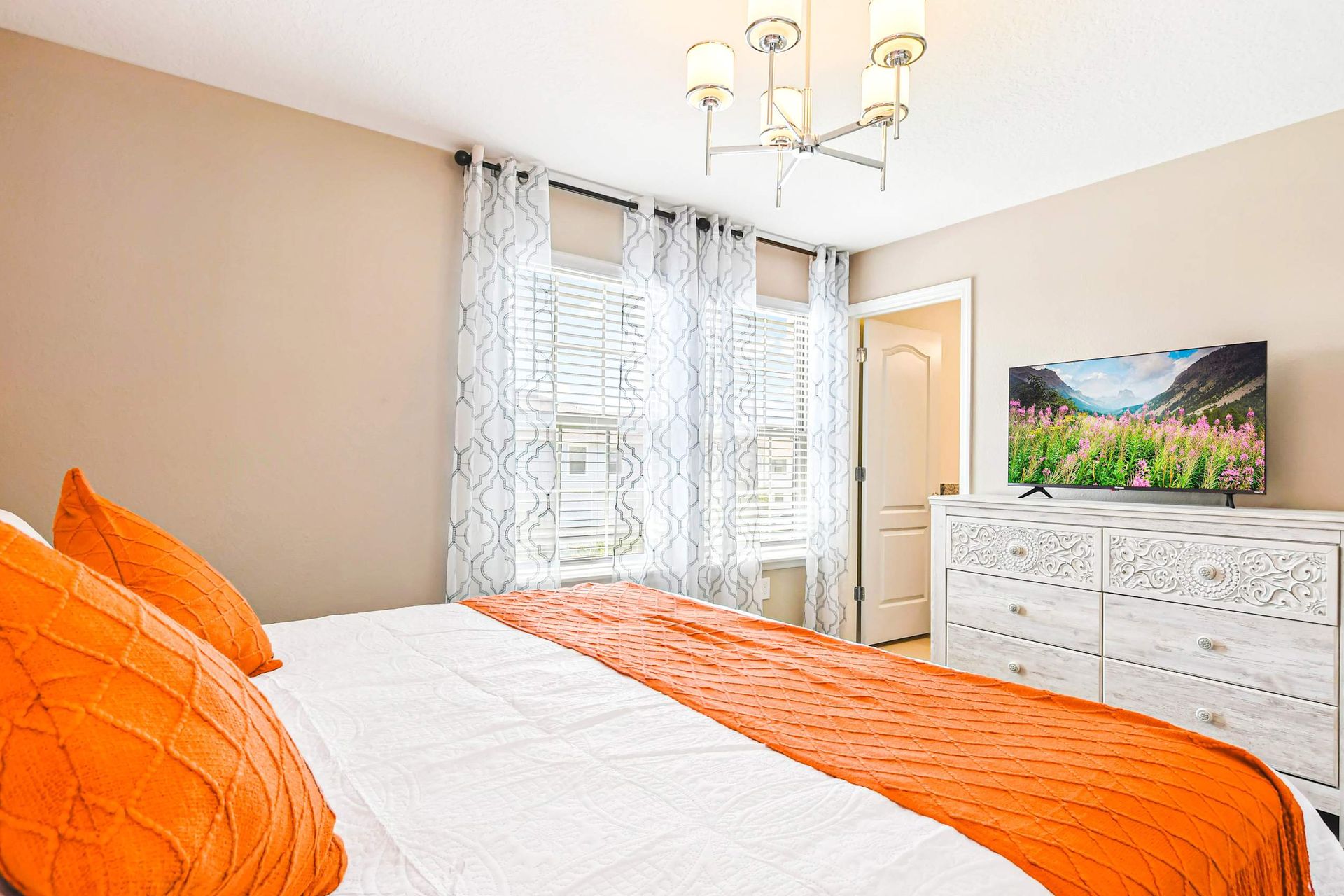 Elegant bedroom with bold orange accents, modern lighting & cozy, luxurious bedding!
