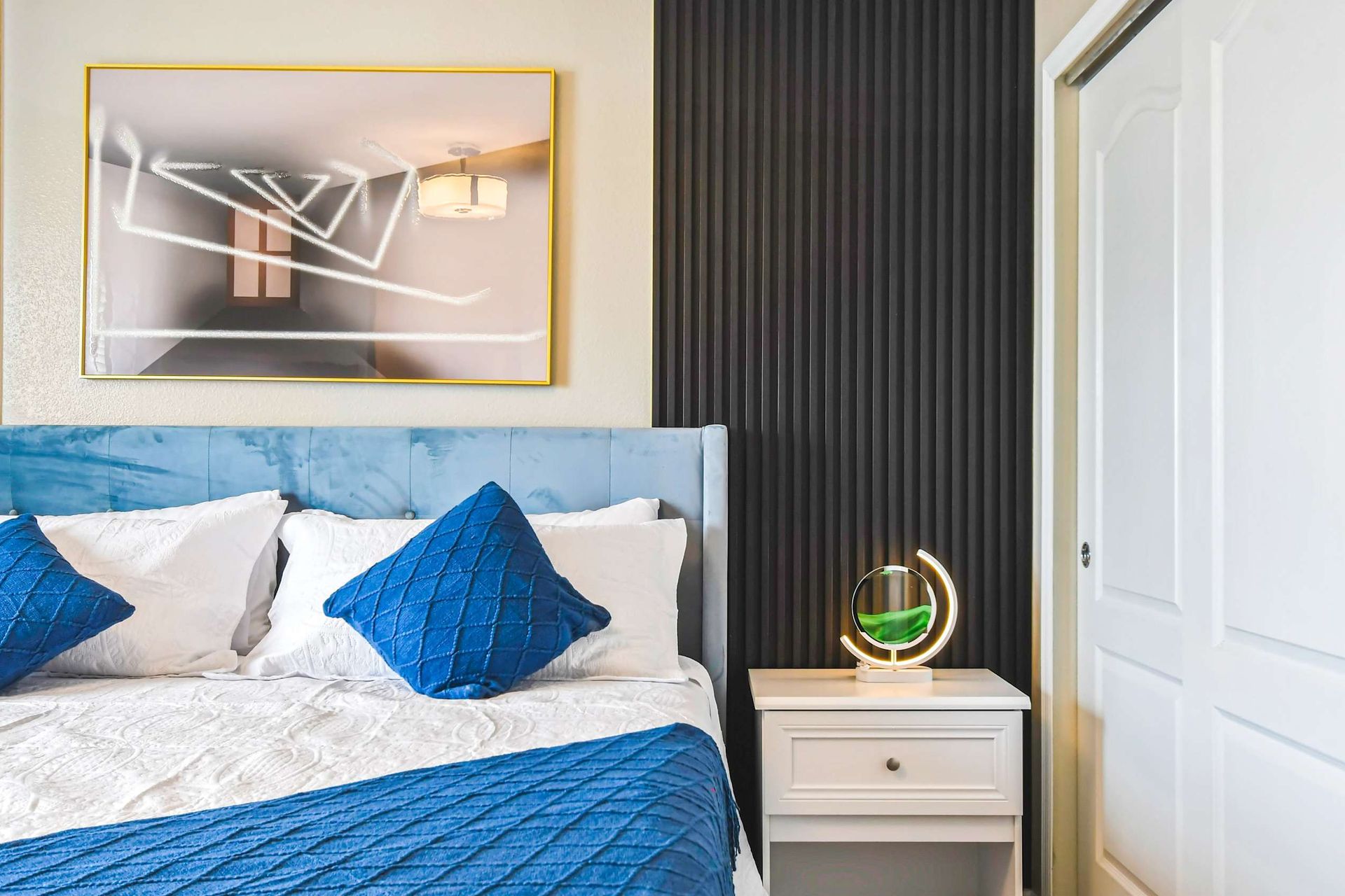 Elegant bedroom with bold blue accents, modern lighting & cozy, luxurious bedding!