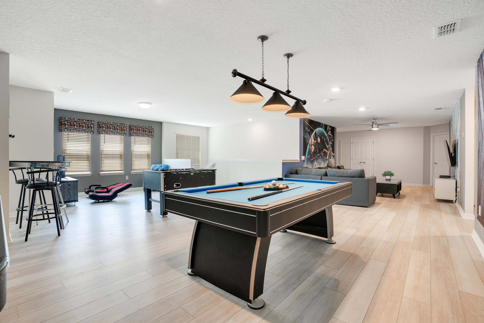 Spacious game room with pool table, foosball, gaming chairs, and seating area.
