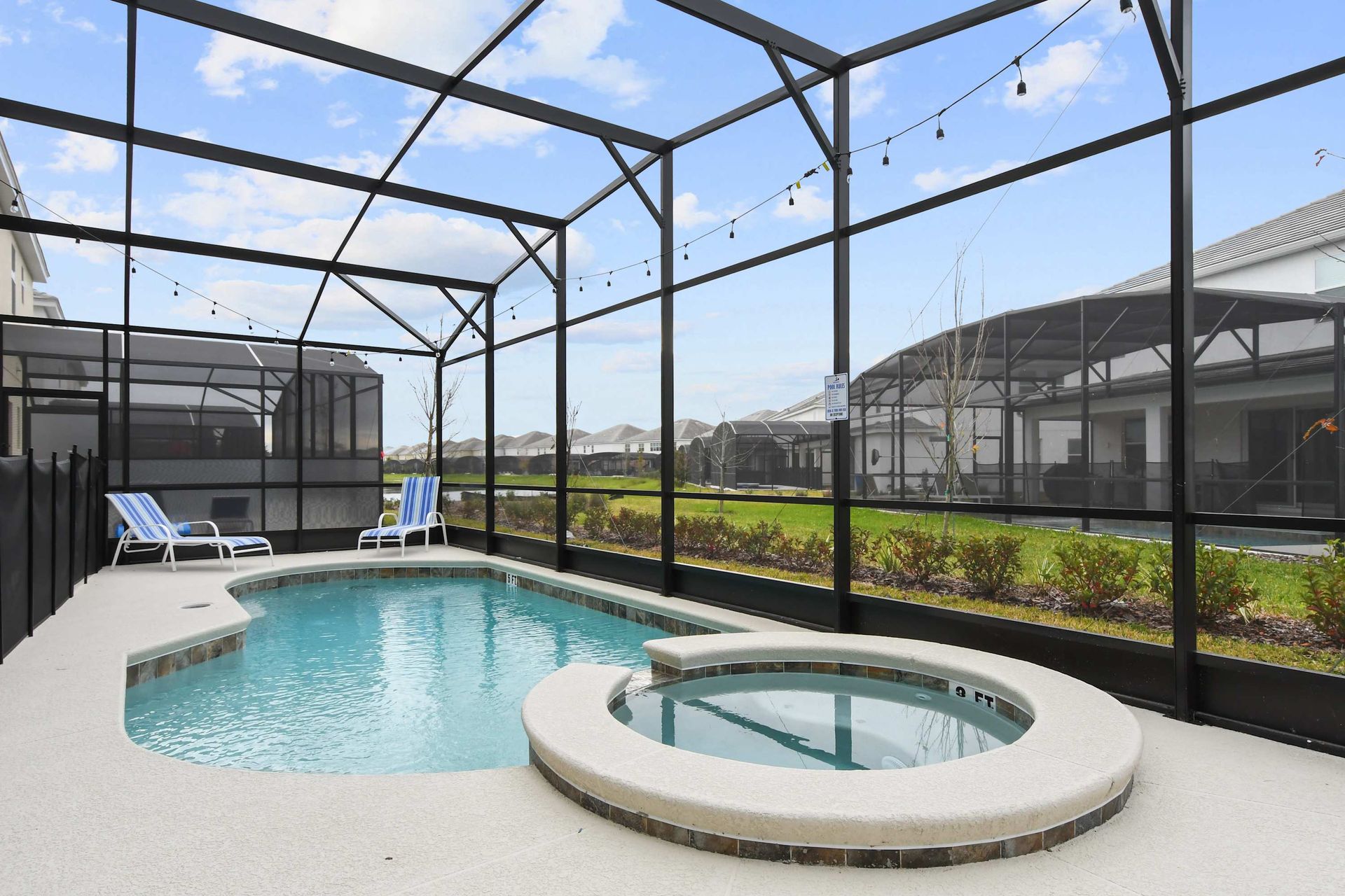 Screened-in private pool and spa with lounge seating, outdoor bar, and string lights.