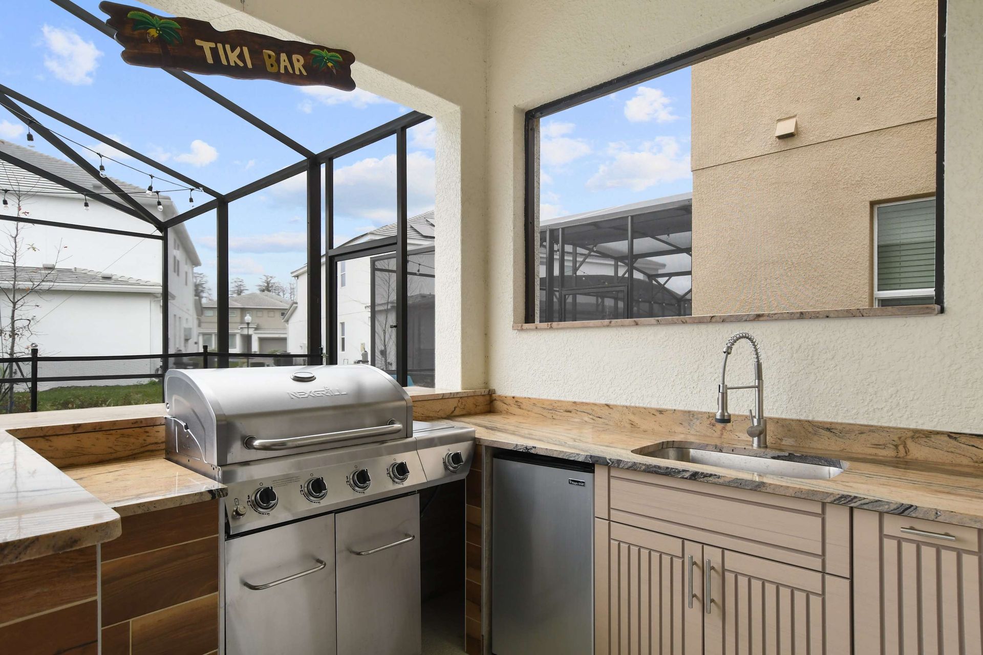 Outdoor tiki bar with a built-in grill, sink, mini fridge, and spacious counter space.