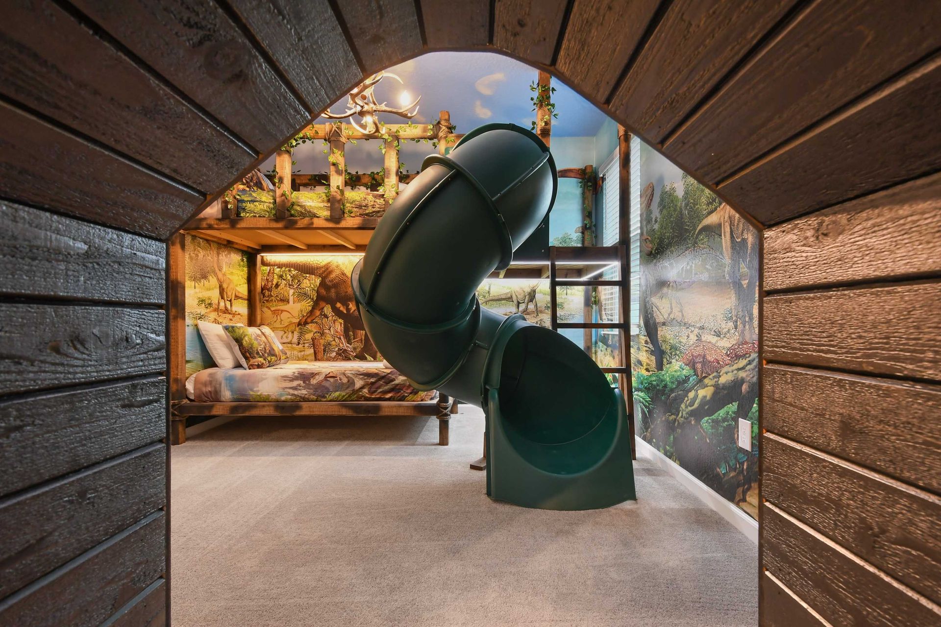 Dinosaur-themed kids' room with a slide, bunk beds, and immersive jungle decor.