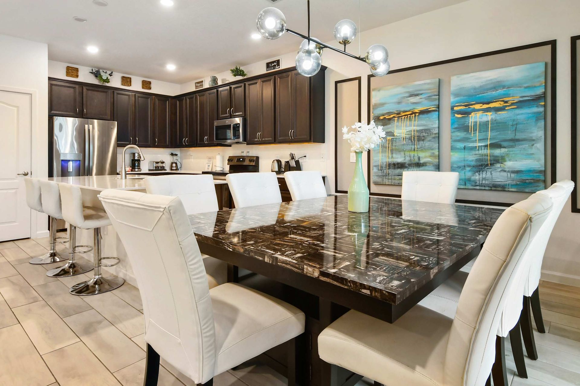 Elegant dining area with a sleek marble table, modern lighting, and a full kitchen.
