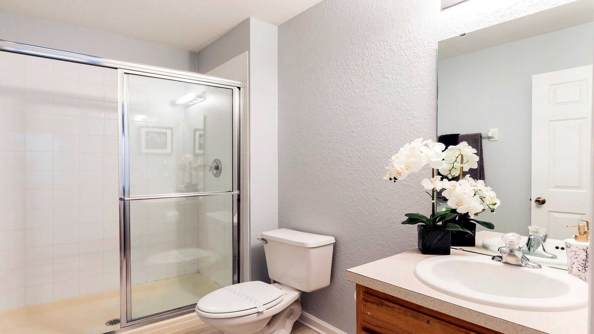 Modern bathroom with glass walk-in shower, bright vanity, and elegant floral décor
