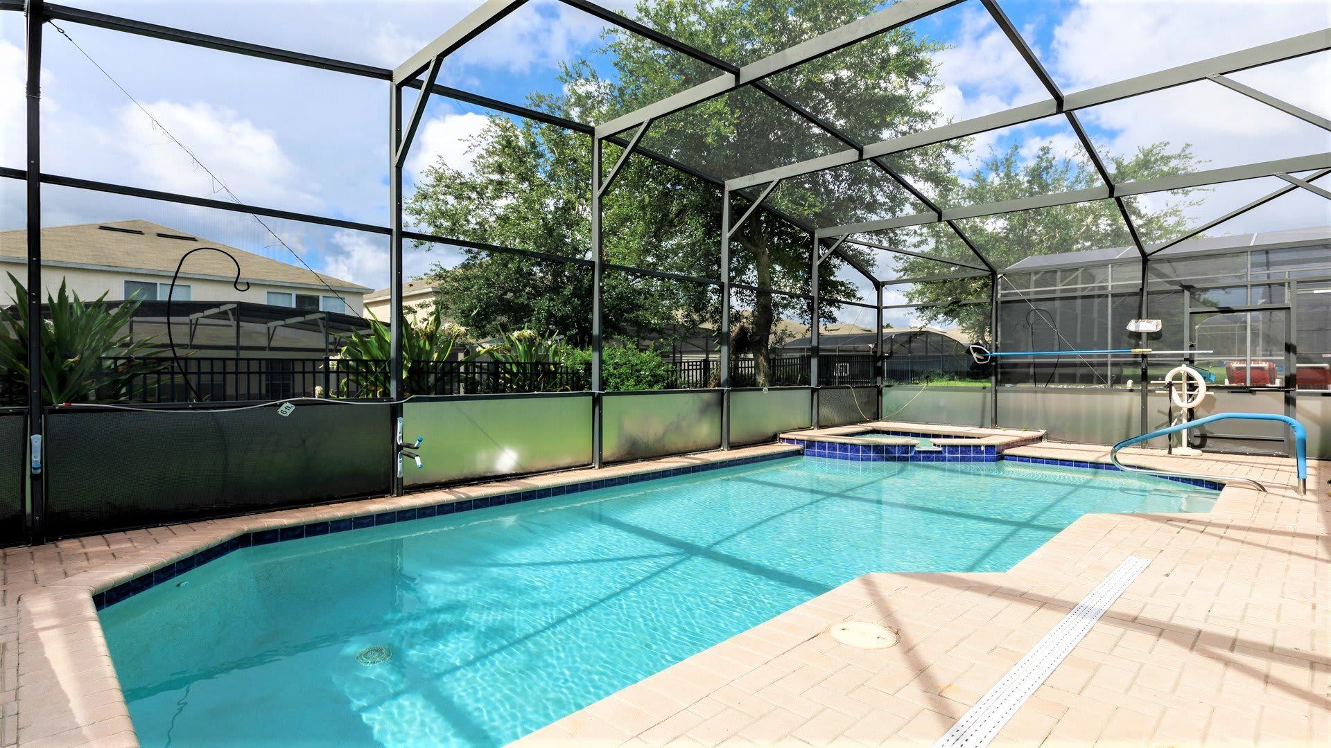 Private screened-in pool with a spa, surrounded by lush greenery and open skies.