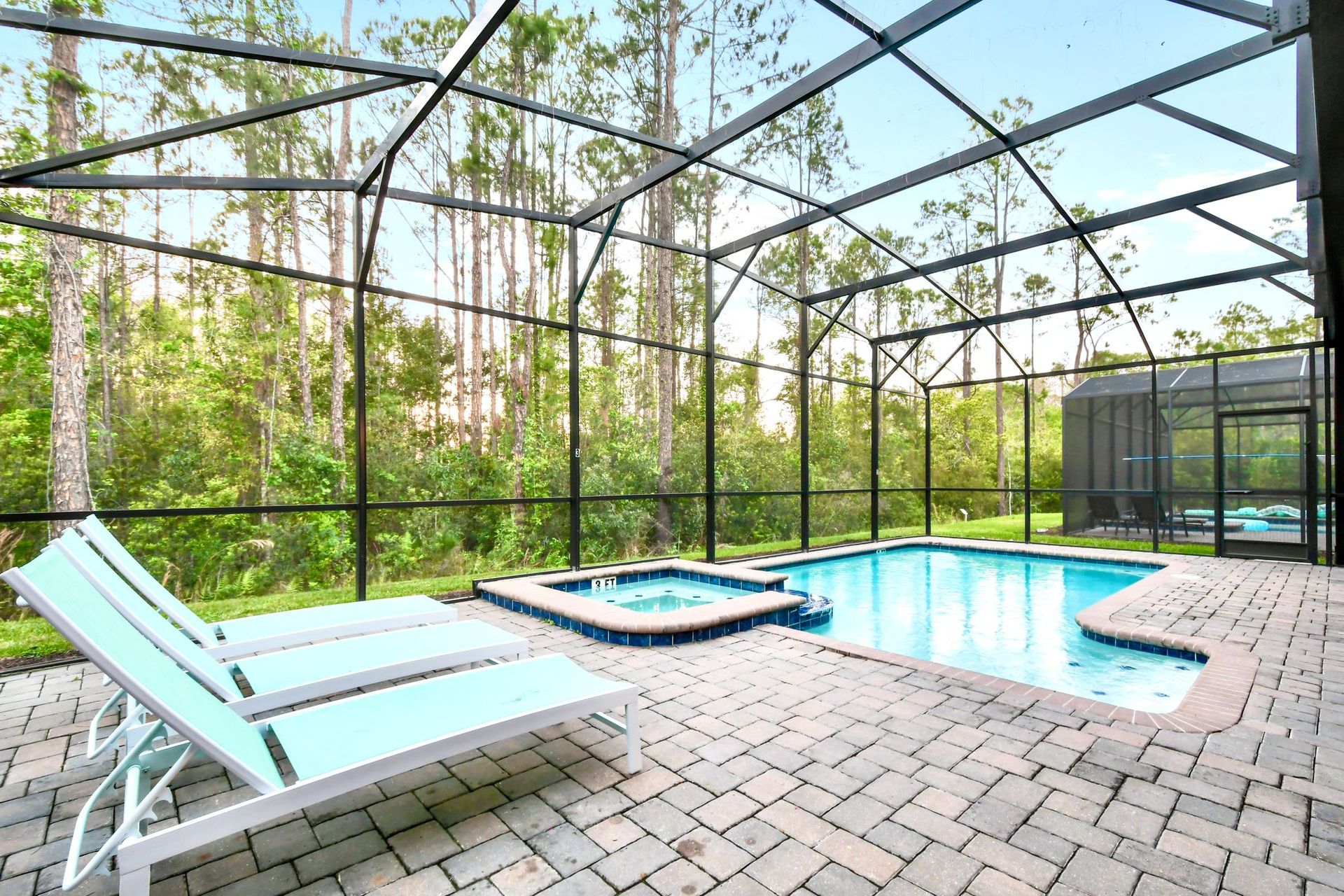 Serene screened-in pool and spa with lounge chairs, surrounded by lush nature views.