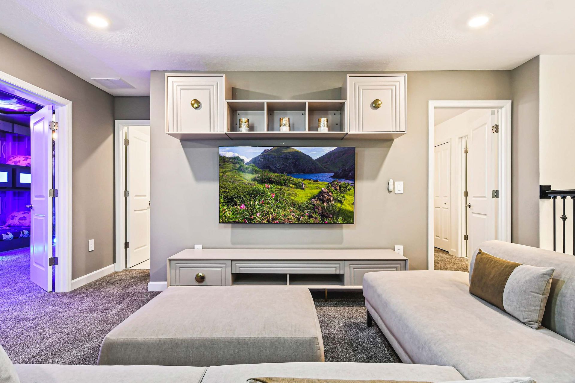 Modern lounge with a plush sectional, large TV, and a futuristic-themed room nearby.