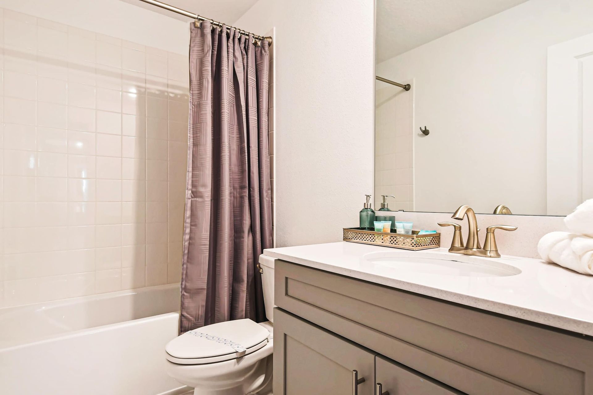 Modern bathroom with a sleek vanity, gold fixtures, and a shower-tub combination.