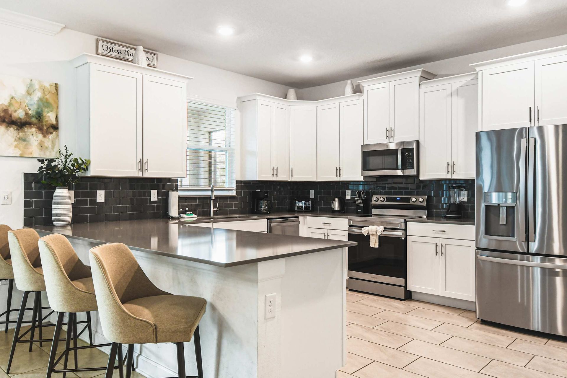 Sleek modern kitchen with stainless appliances, big island, bar seating and bright light
