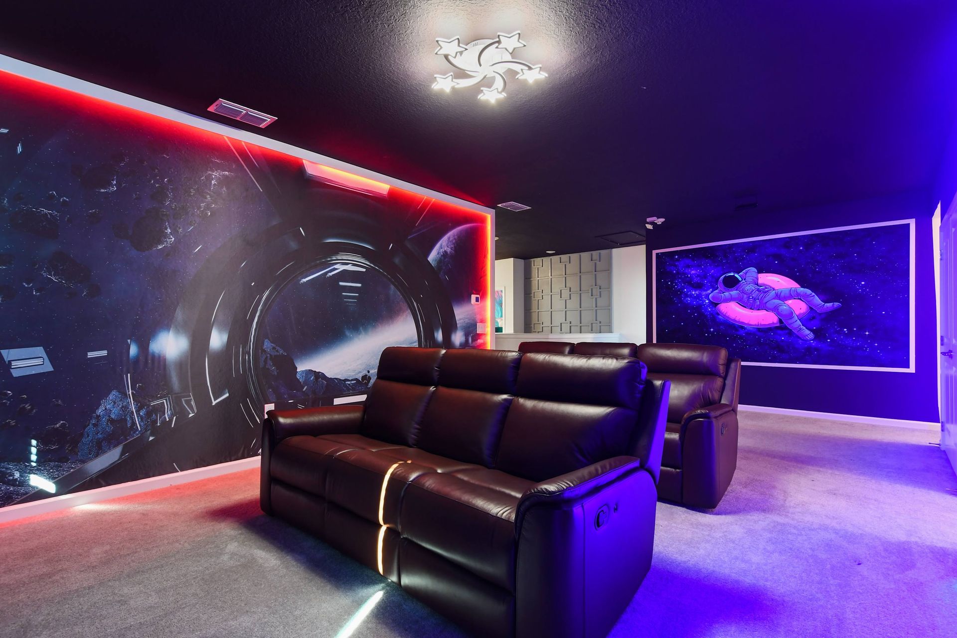 Space-themed home theater with reclining seats, ambient lighting, and cosmic art.