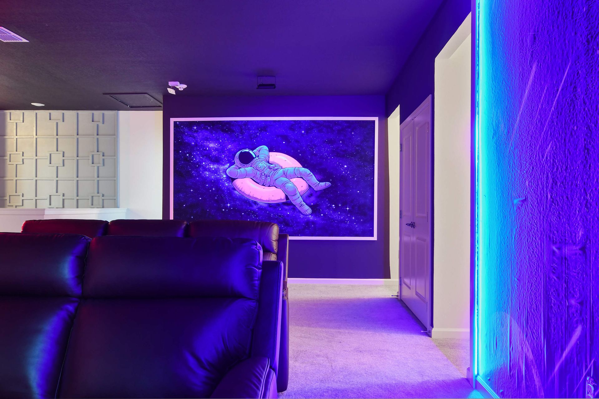 Futuristic theater room with neon lighting, cosmic art, and cozy seating.
