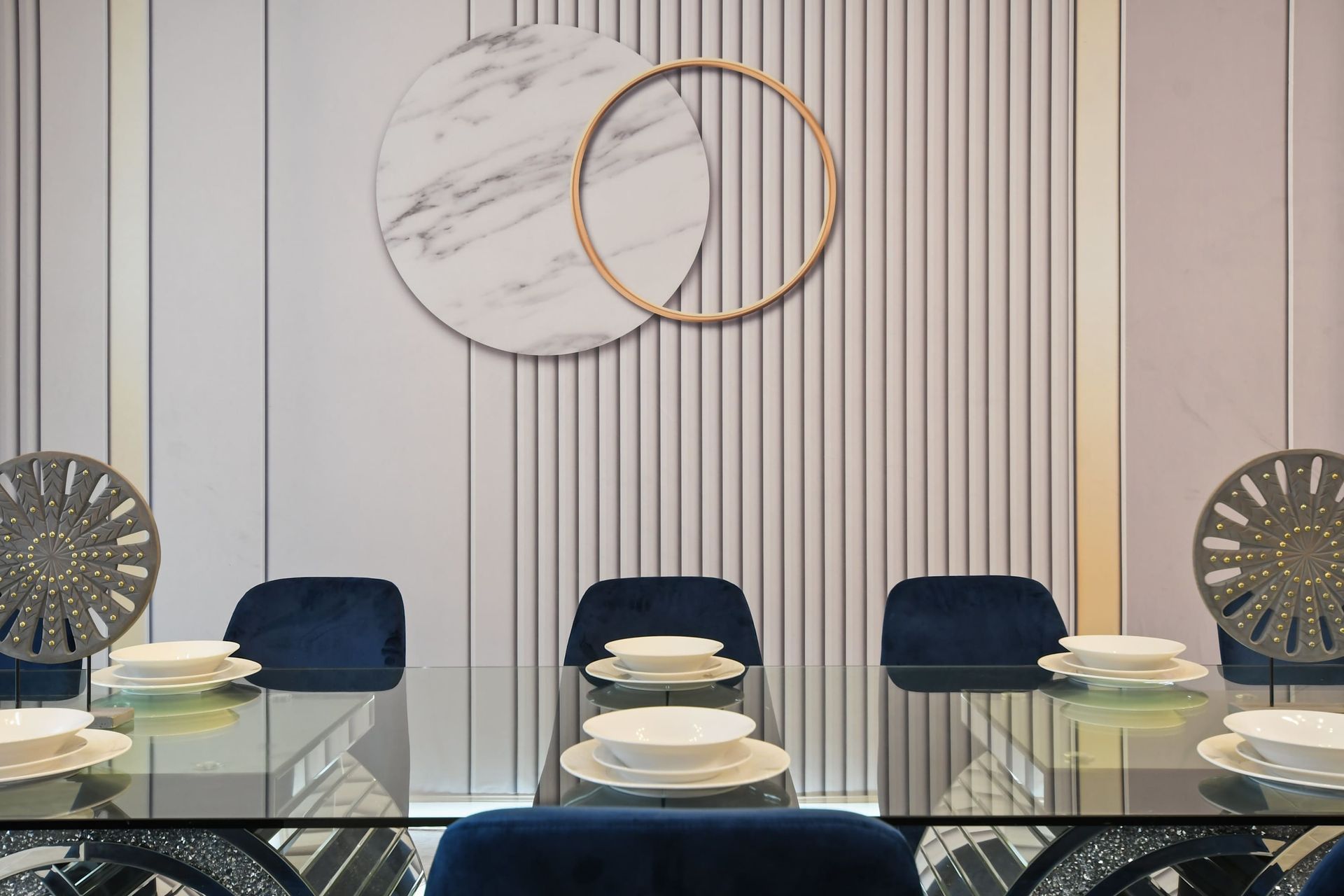 Elegant dining setup with marble-inspired art, glass table, and navy seating.