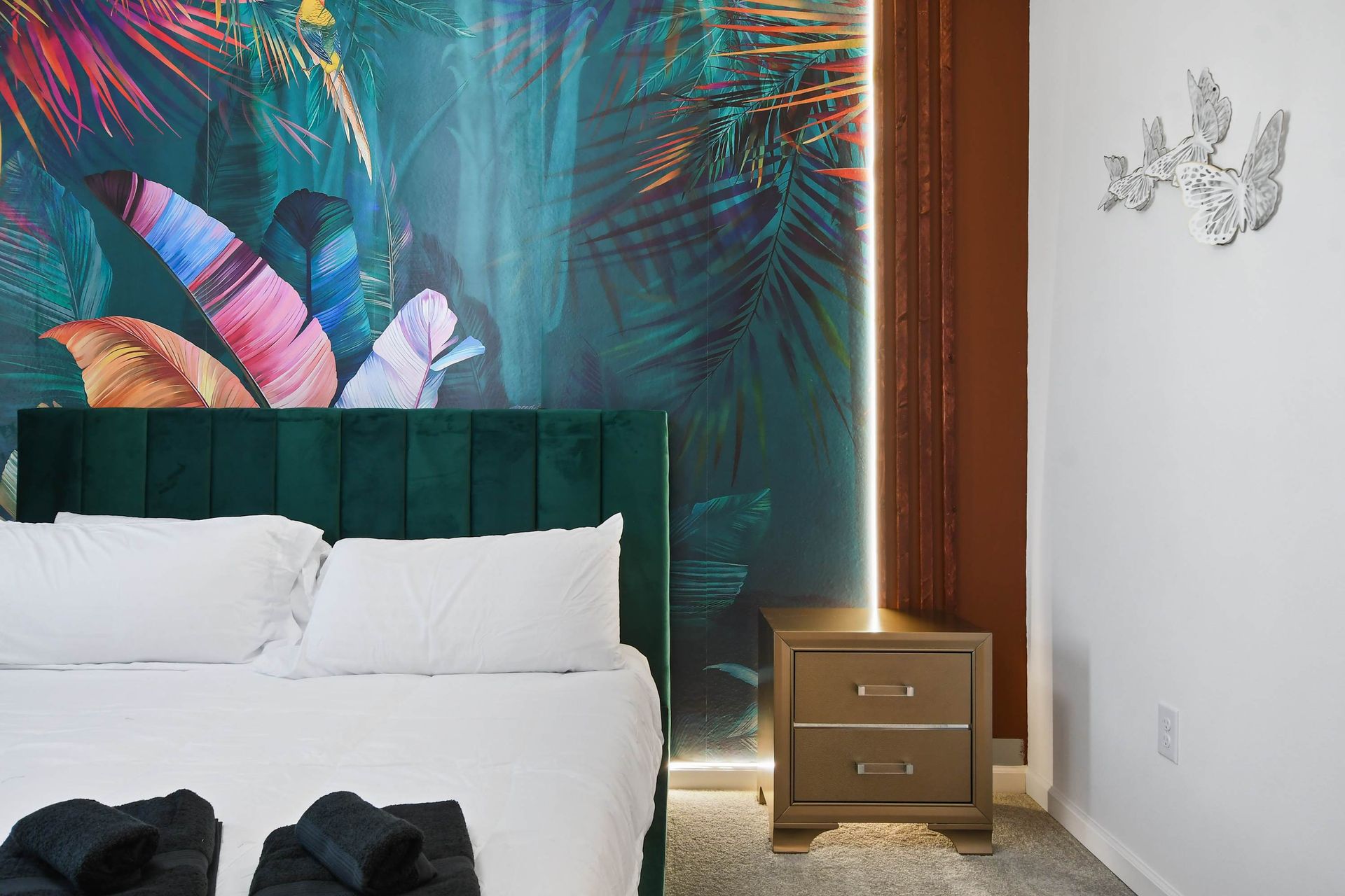 Tropical-themed bedroom with lush mural, velvet bed, and elegant lighting.