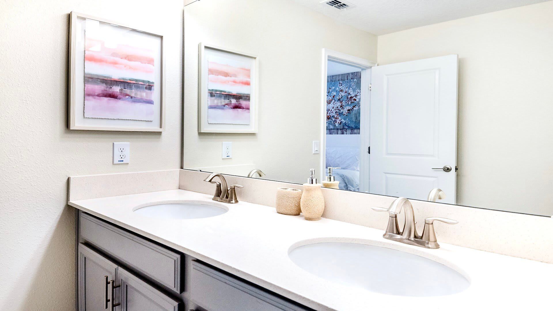 Bright en-suite bathroom with double vanity, soft pastel art, and modern finishes