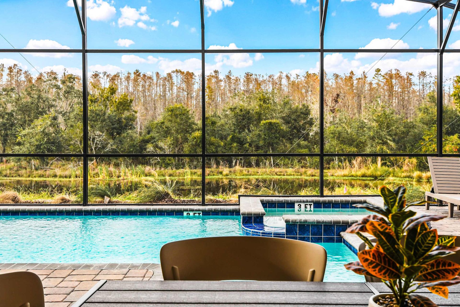 Screened-in pool with spa, forest views, and serene outdoor dining space.