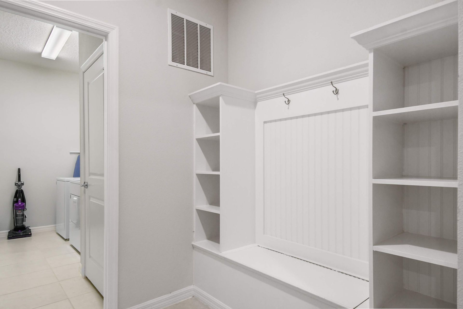 Bright mudroom with built-in bench, hooks, open shelves and convenient laundry access
