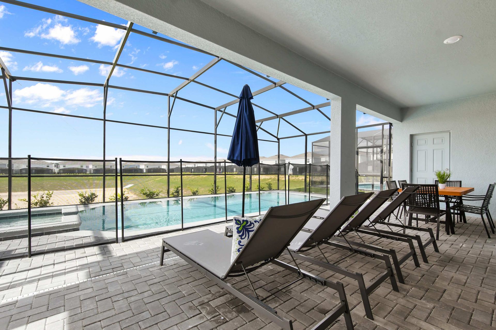 Relaxing screened-in pool and spa with sun loungers, dining table, and open views