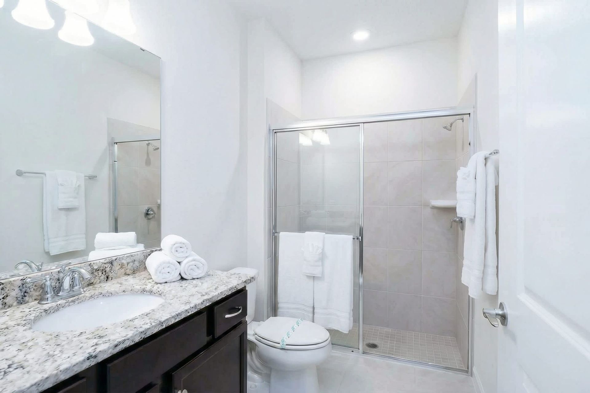 Modern bathroom with granite vanity, glass walk-in shower, and bright lighting.