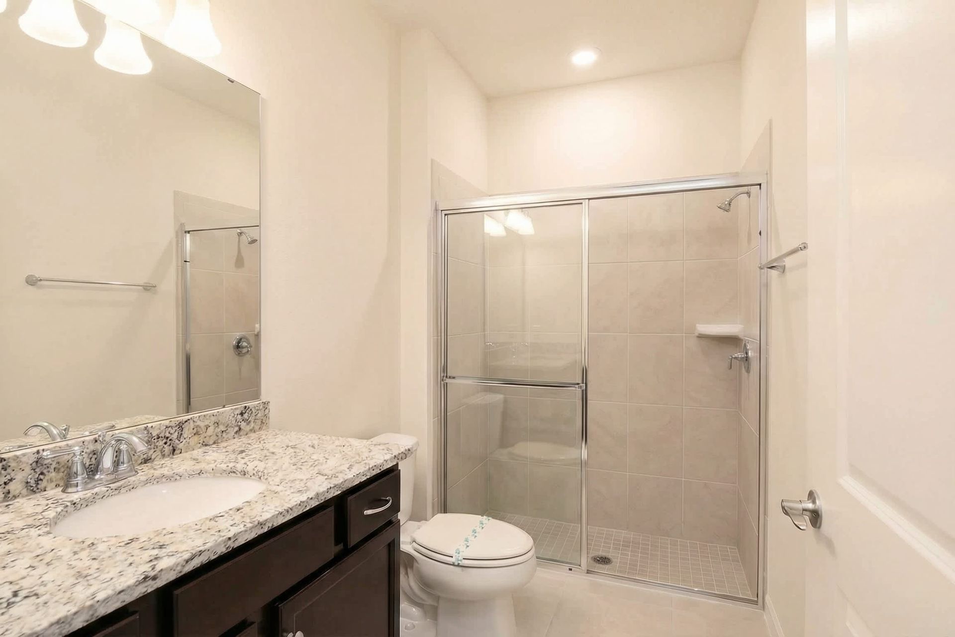 Modern bathroom with granite vanity, glass walk-in shower, and bright lighting.