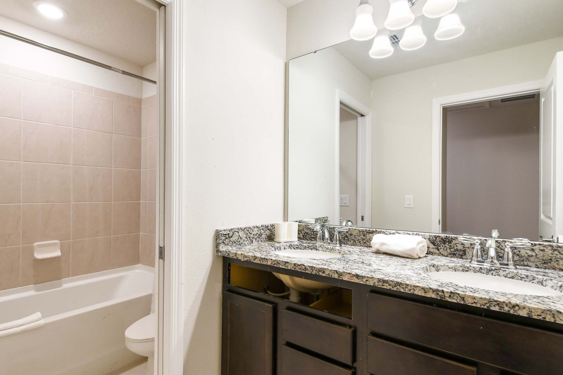 Bright modern bathroom with double granite sinks, large mirror, and tiled shower

