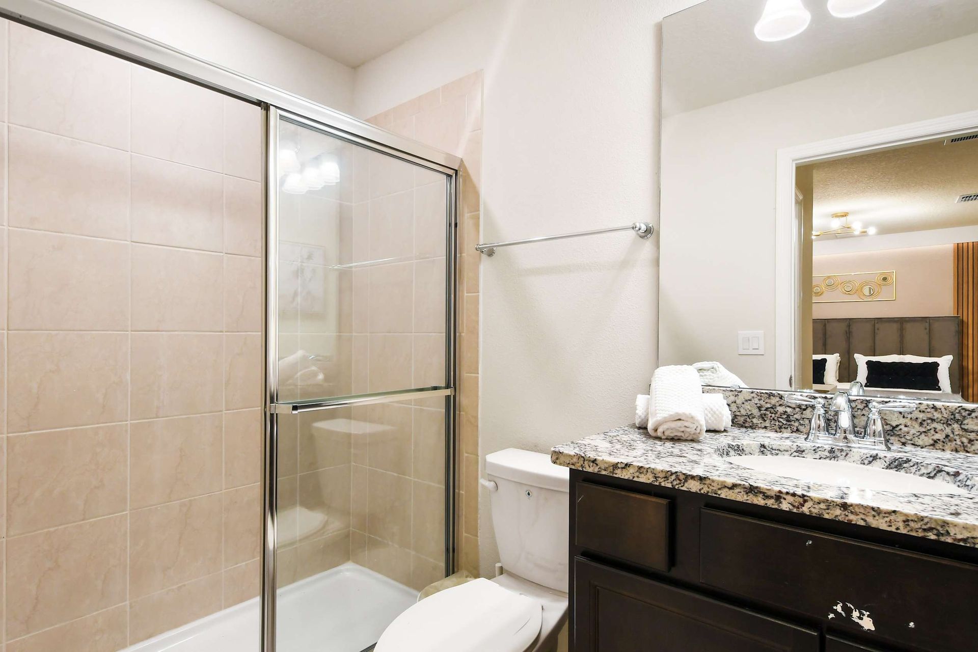 Modern bathroom with granite vanity, glass shower, and view into elegant bedroom
