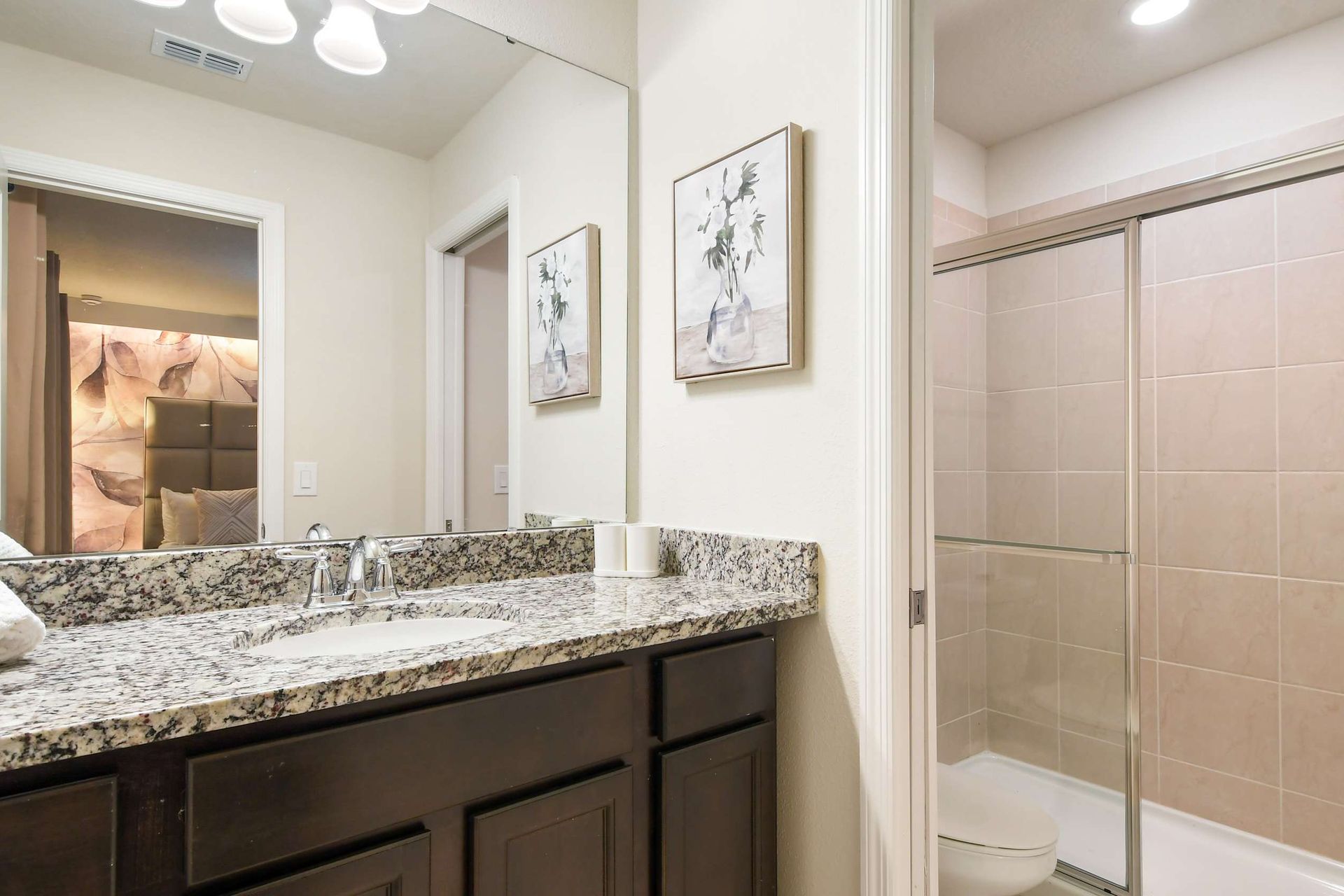 Chic bathroom with granite vanity, glass shower, soft lighting, and cozy bedroom view
