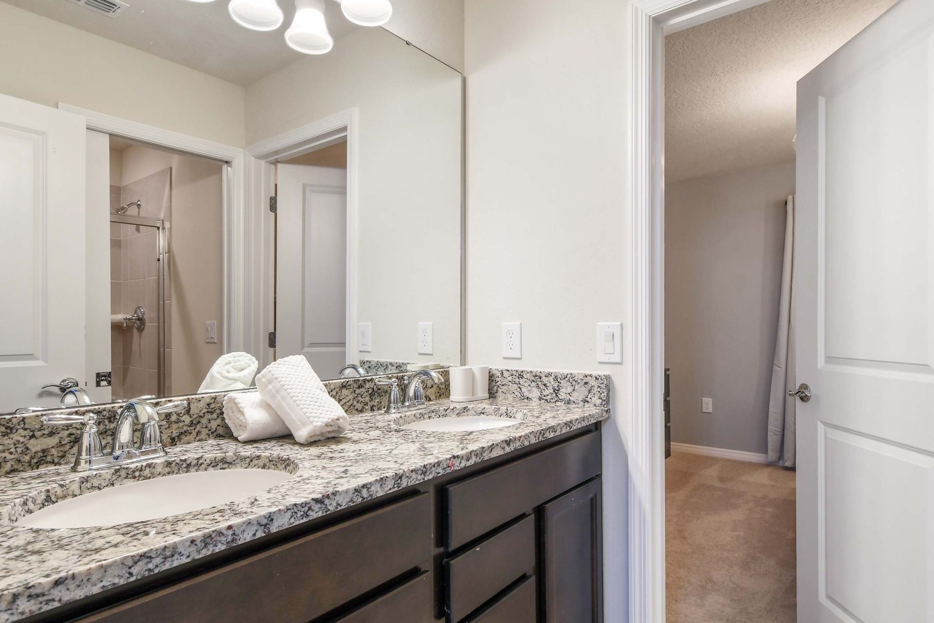 Bright bathroom with double granite vanity, large mirror, and walk-in shower nearby
