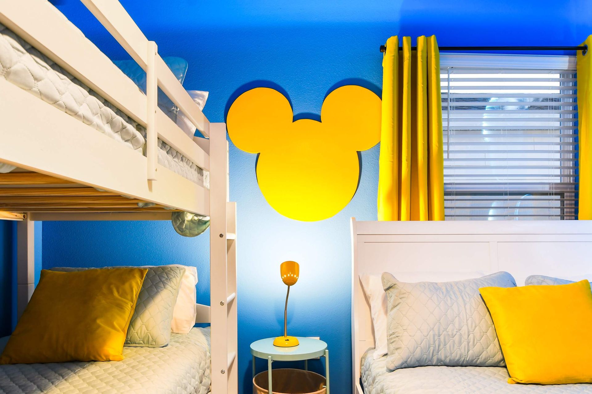 Vibrant Mickey-themed kids’ room with bunk beds, bold blue walls, and sunny accents
