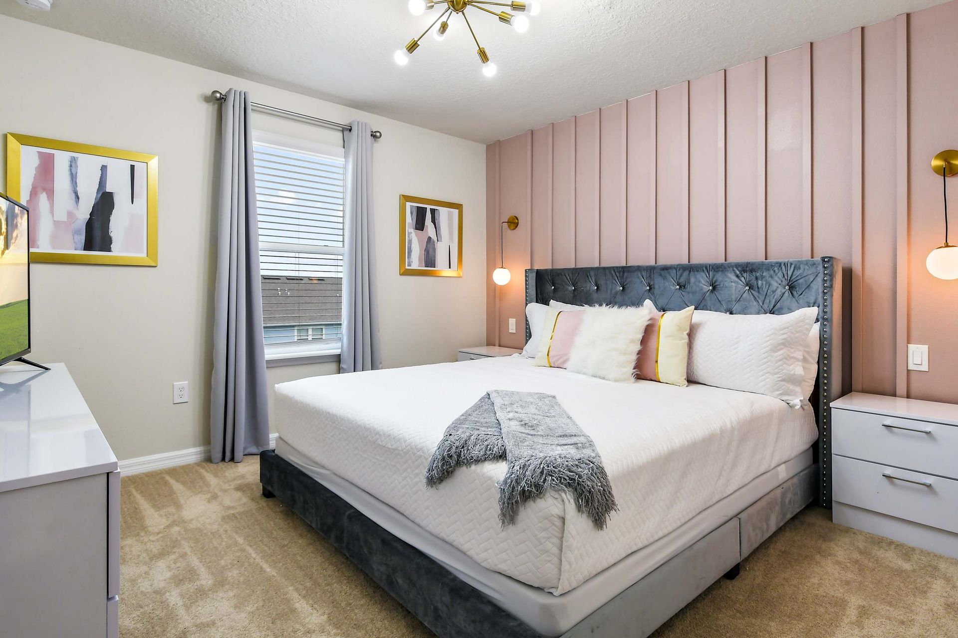 Charming bedroom with blush accent wall, plush king bed, modern lighting, and TV!
