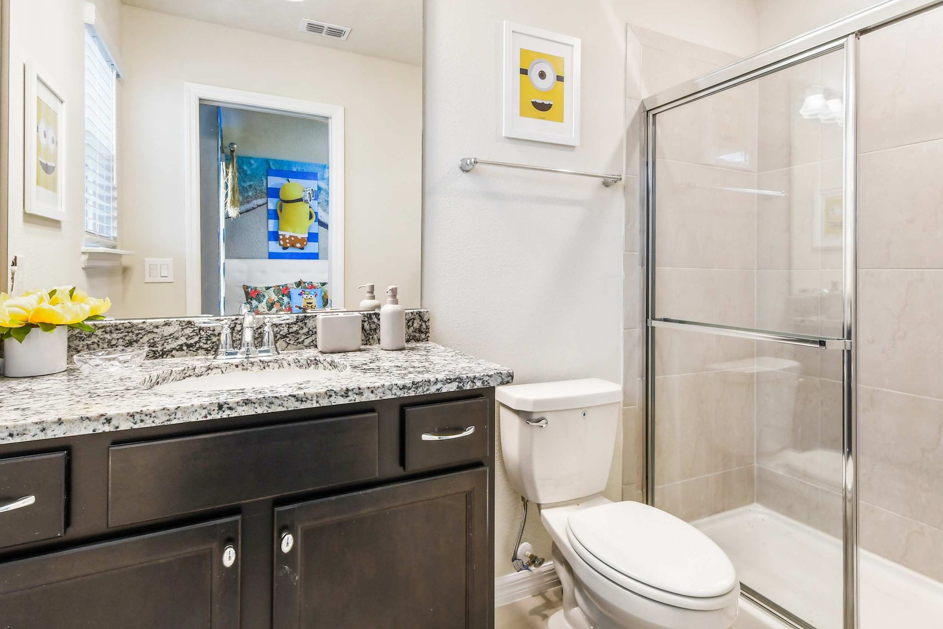 Bright bathroom with granite vanity, glass shower, and fun Minion-themed decor

