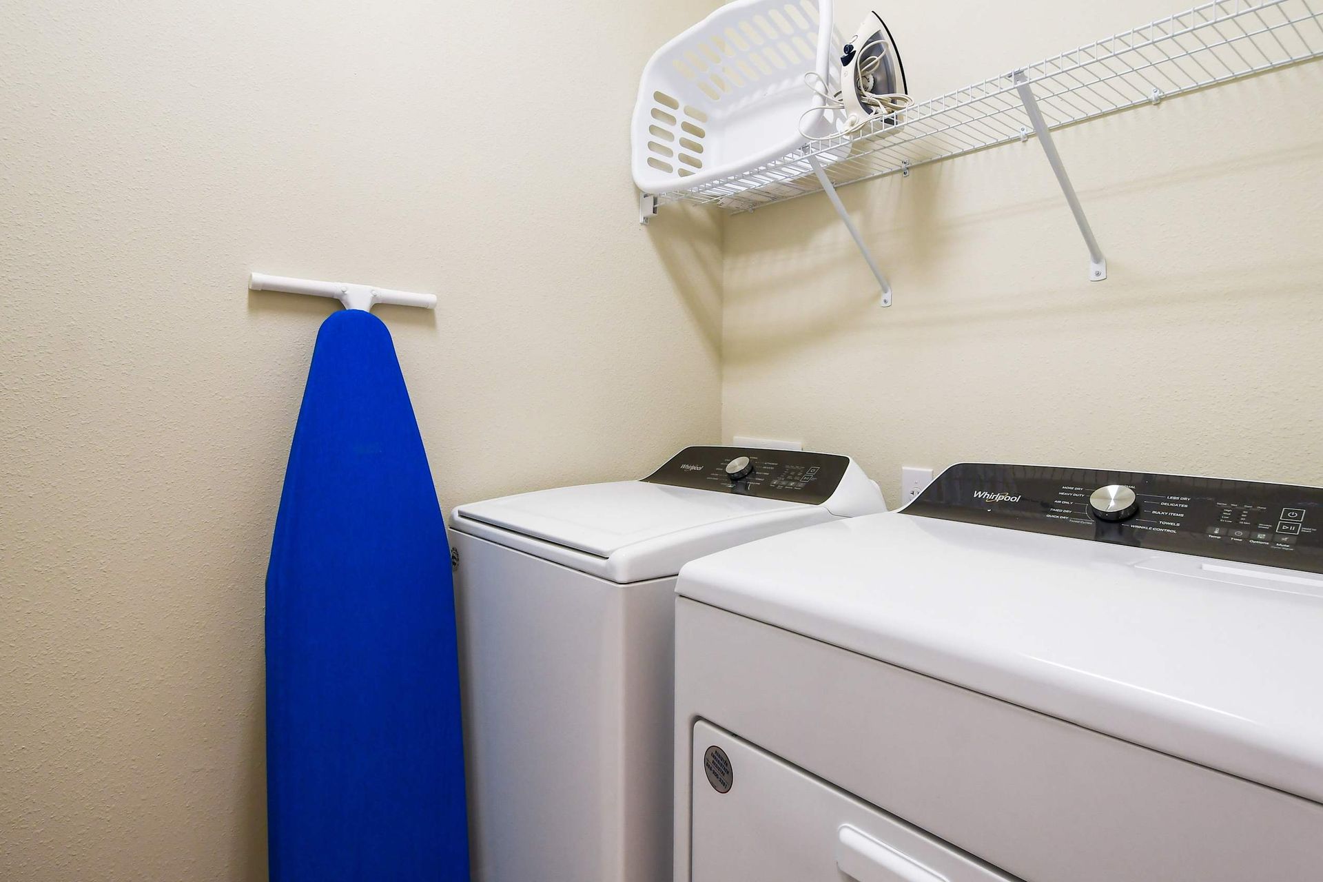 Convenient laundry room with washer, dryer, ironing board, and storage shelf

