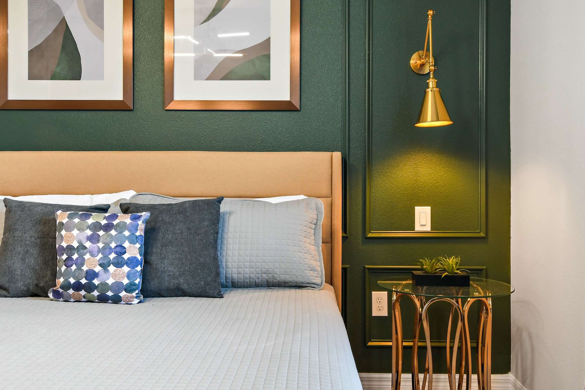 Chic bedroom corner with plush pillows, gold accents, and a deep green feature wall!
