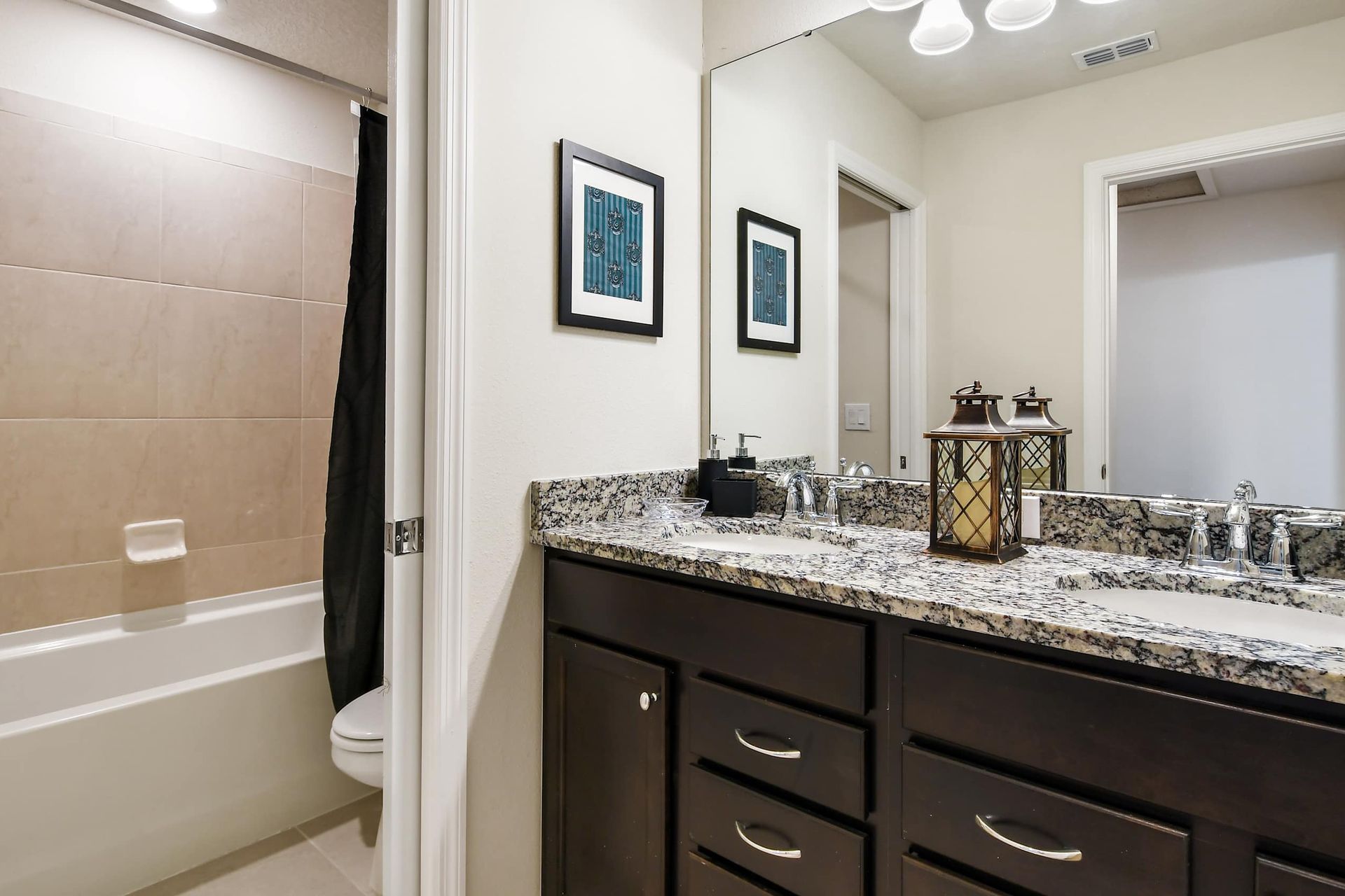 Modern bathroom with granite double vanity, tub shower combo, and elegant decor
