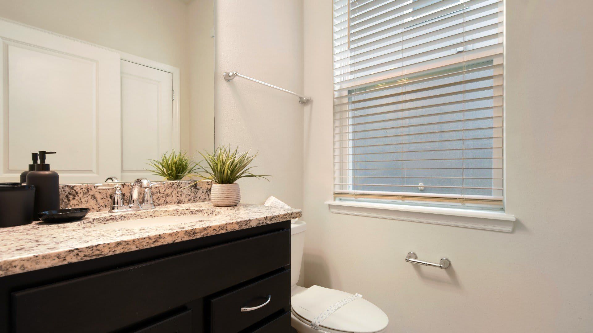 Bright and stylish half bath with granite vanity, sleek fixtures, and natural light.