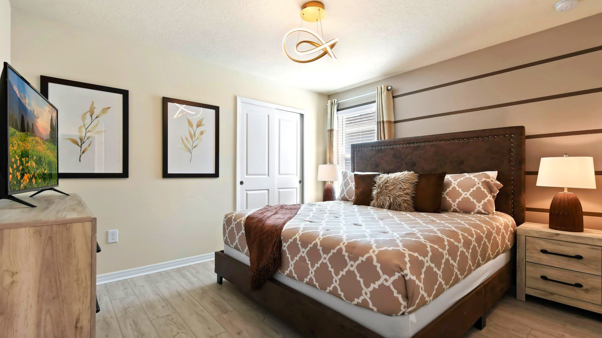 Warm and inviting king bedroom with modern décor, TV, and natural light.