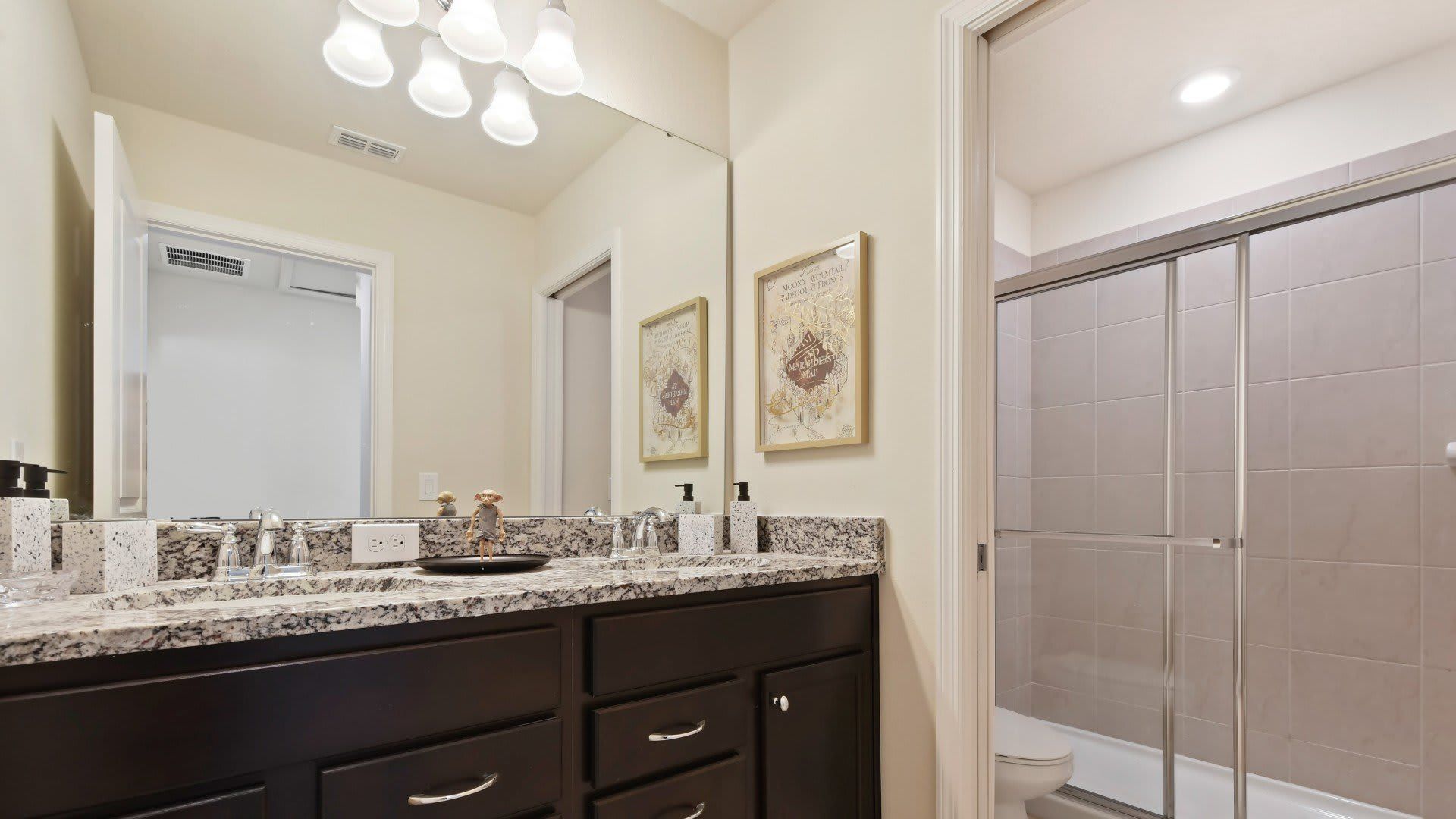 Chic granite bathroom with double vanity and walk-in shower near themed bedrooms.