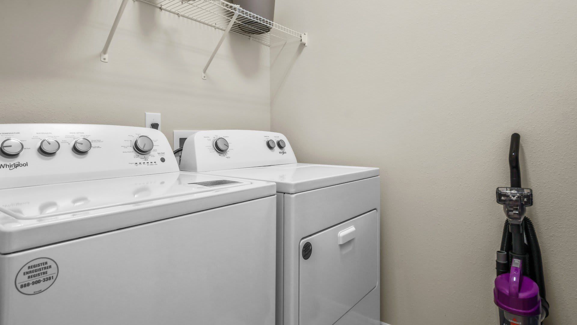 Full laundry room with washer, dryer, vacuum, and shelving for essentials.
