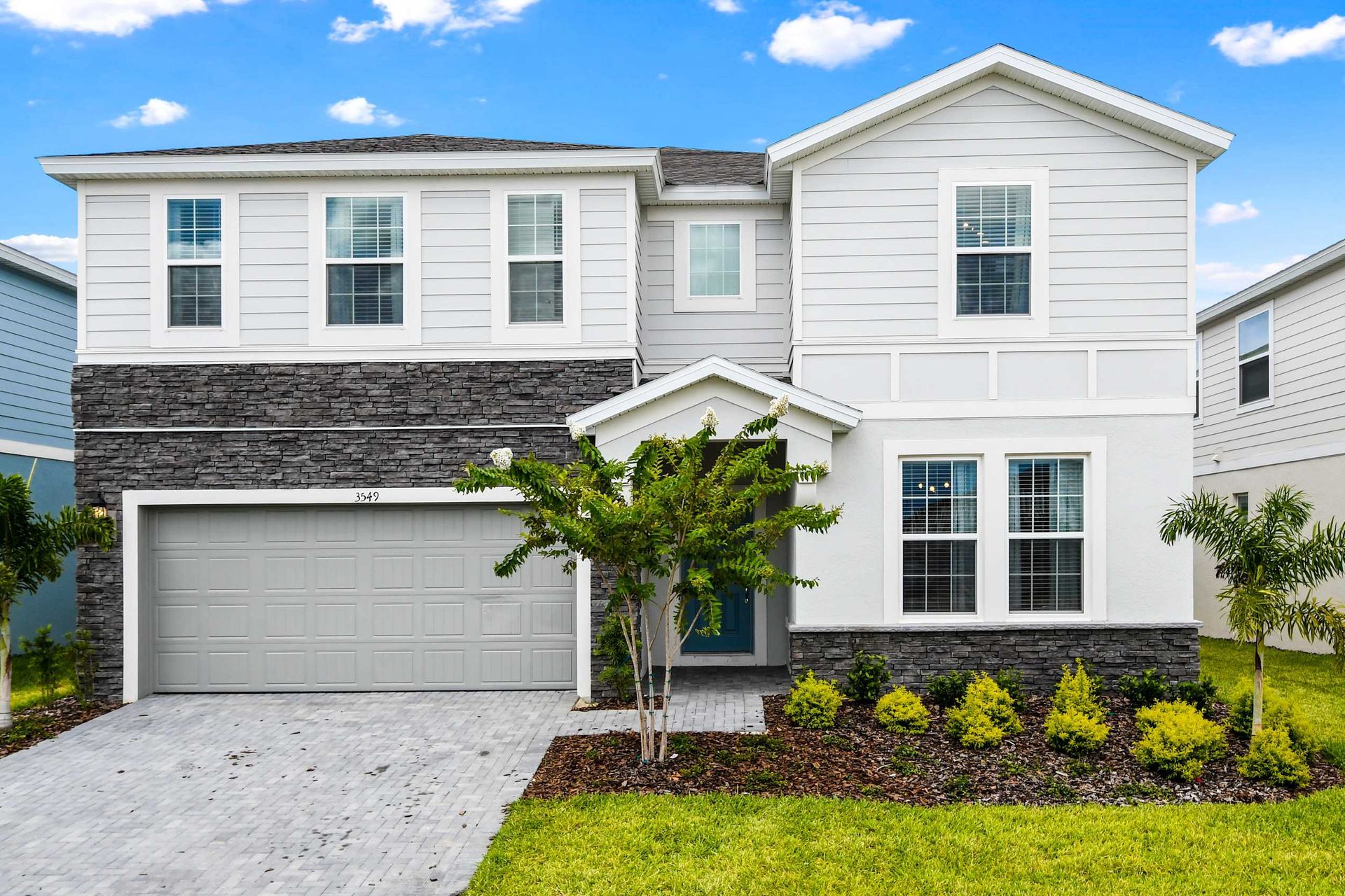 Modern two-story villa with stone accents, lush landscaping, and spacious garage
